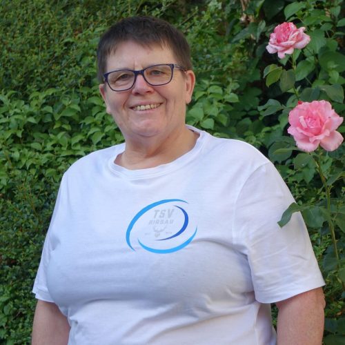 Christa vom TSV Hirsau steht vor einer blühenden Hecke und lächelt freundlich in die Kamera